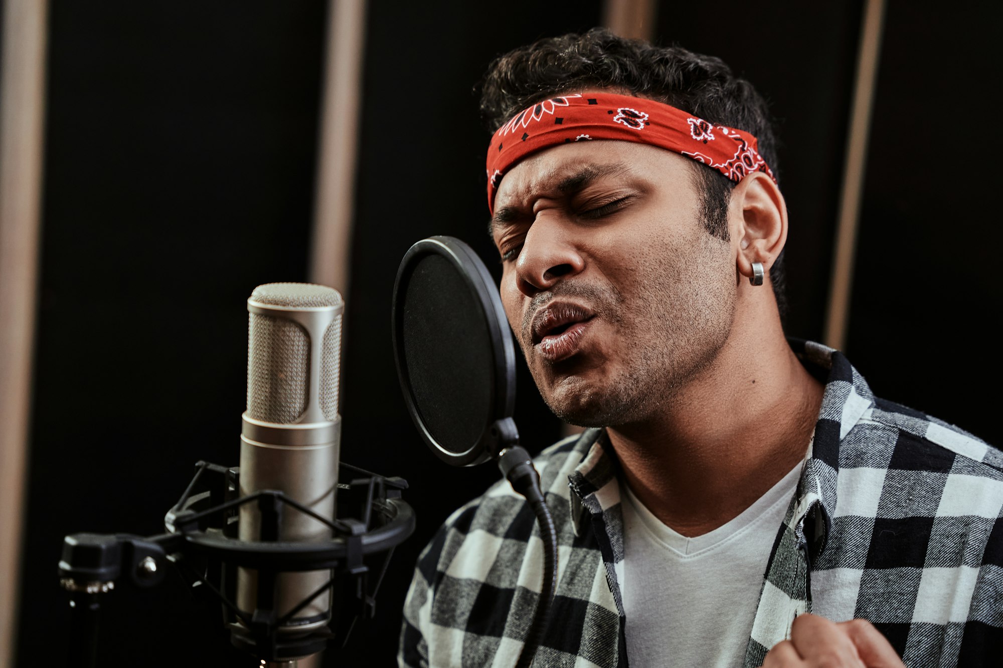 Portrait of young man, hip hop artist looking focused, singing into a condenser microphone while